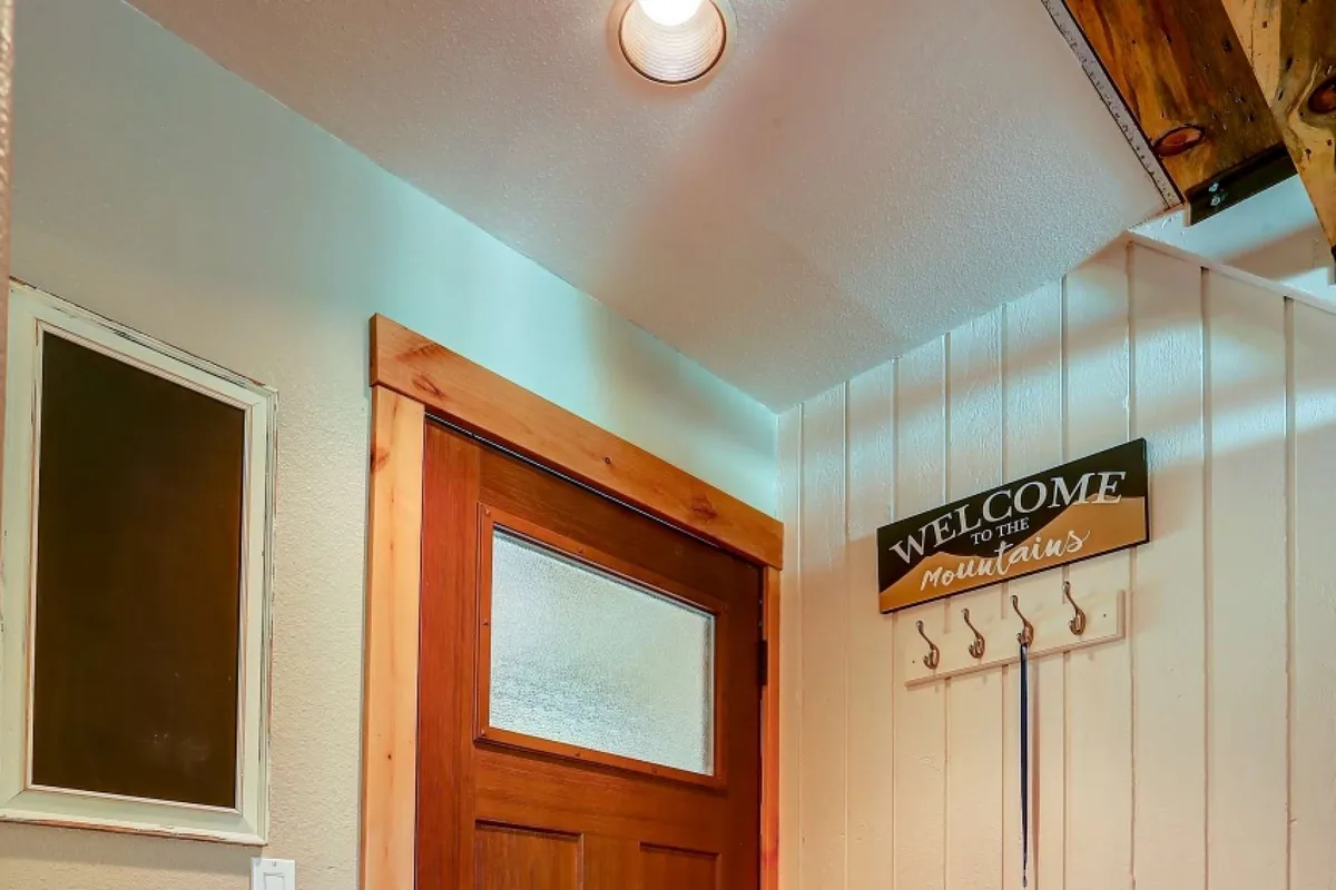 A warmly lit entryway welcomes guests with a rustic wooden door, a friendly welcome sign, and a large mirror reflecting the cozy ambiance. There's space for hanging coats and taking off shoes, suggesting the beginning or end of a memorable outing.