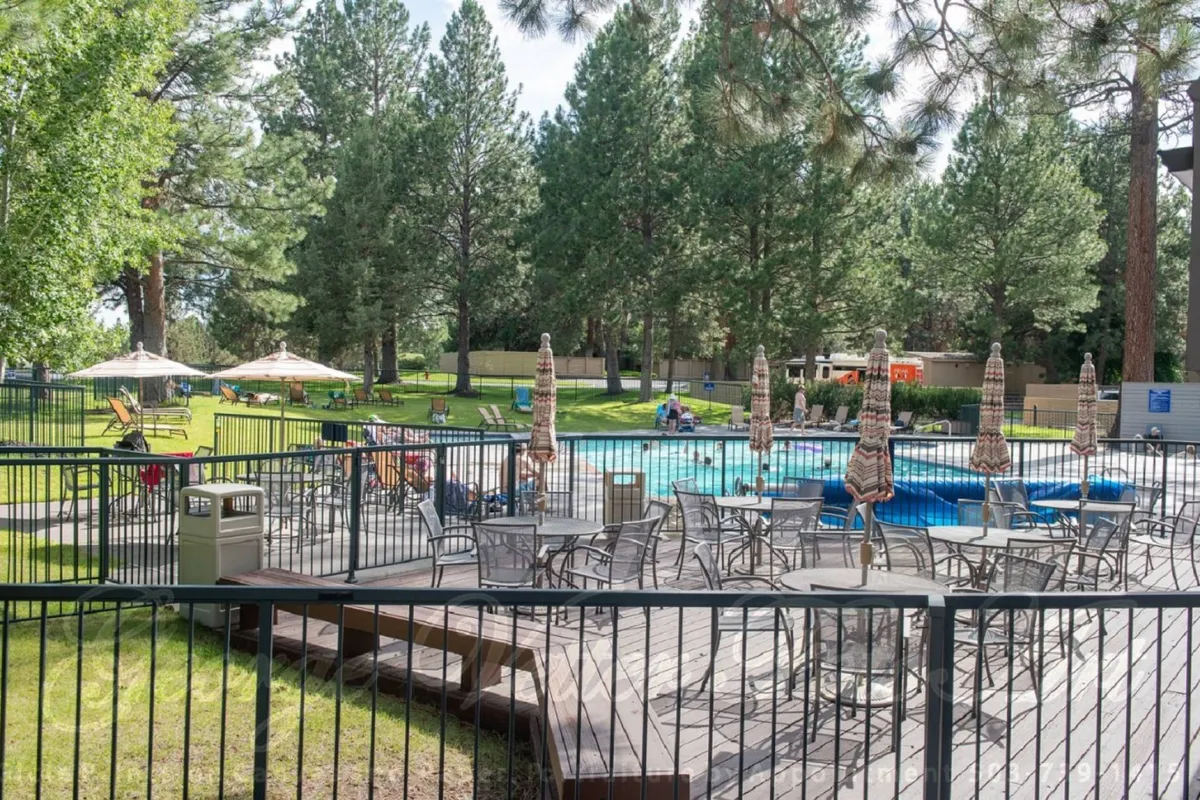 A sparkling swimming pool is bordered by lounge chairs and umbrellas, with a green lawn and tall trees creating an inviting backdrop. Families and friends are seen relaxing and socializing, reflecting an atmosphere of leisure and inclusivity.