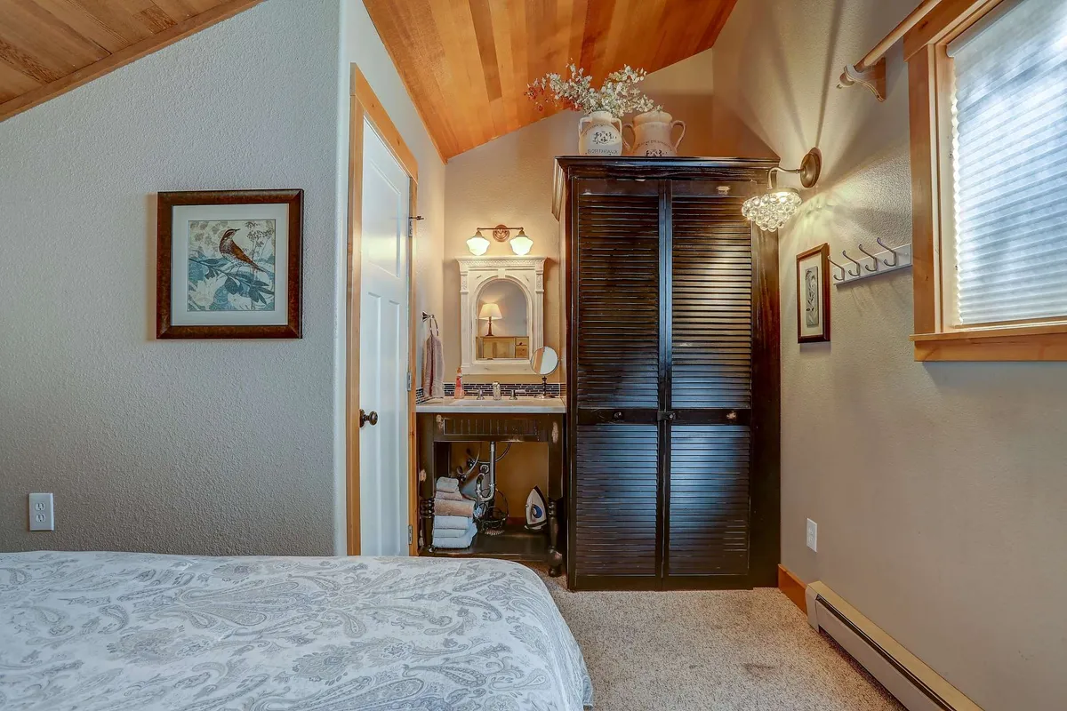 A cozy bedroom with patterned bedding, a dark wooden cabinet adorned with decorative items, and a wall-mounted mirror. Sunlight streams in, creating an intimate, serene atmosphere perfect for unwinding after exploring the outdoors.