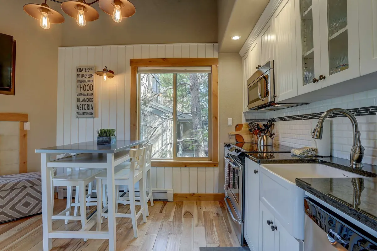 A bright kitchen and dining space featuring contemporary appliances, a sunlit window, decorative wall art, and a well-set dining table and chairs. The area exudes warmth and is ideal for socializing and sharing meals.
