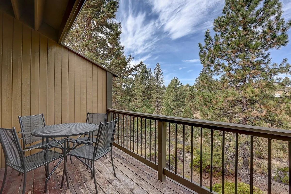 An exterior view of a private deck featuring an outdoor dining set surrounded by lush greenery and mountain views. The space is set for morning coffee, alfresco dining, or relaxed evening BBQs, highlighting the peaceful connection to the outdoors.