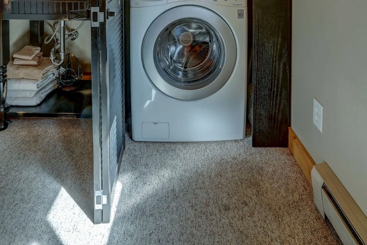 A neatly organized laundry nook with a washing machine and shelves stacked with fresh towels. The design is practical and home-like, ensuring convenience for guests.